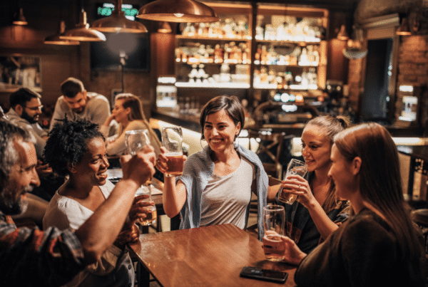 Group of friends raising pints of beer at a busy, dimly lit bar, a reminder of the liability that comes with serving alcohol.