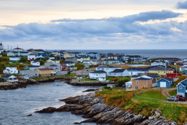 Colourful houses along a rocky harbour in Channel-Port aux Basques, Newfoundland, with the ocean and a cloudy evening sky behind them.